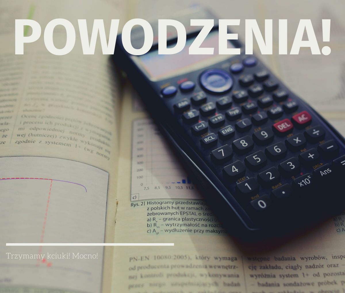 Kalkulator naukowy leżący na podręczniku. Na wierzchu napisa 'Powodzenia!'